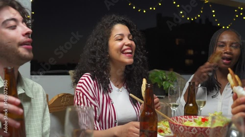 three young Latin friends happily share a dinner eating empanadas on a terrace at dusk
