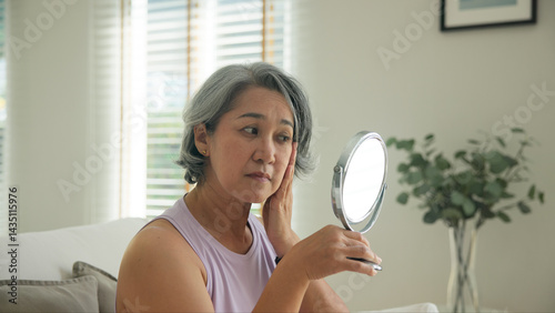 Asia adult people middle age old woman look at mirror dry skin face hand touch neck cheek stress sad at home elder health care aging beauty issue. Asian female aged eye botox filler plastic surgery.