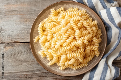 Bowl of uncooked fusilli pasta on rustic wooden table with striped fabric