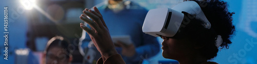 Individual wearing VR headset engrossed in virtual reality experience with soft focus on surrounding environment indicating collaborative and technological atmosphere