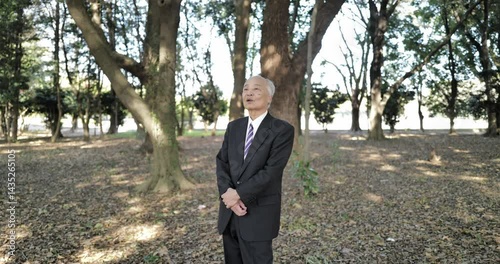 In a cold park in Japan in March, a man in his 70s, in a suit, stands and talks. Surrounded by crisp early spring air and peaceful nature, he shares his thoughts quietly in the calm surroundings.