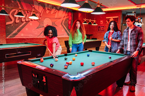 Group of young multicultural friends playing billiards in a bowling alley entertainment center, enjoying their leisure time together