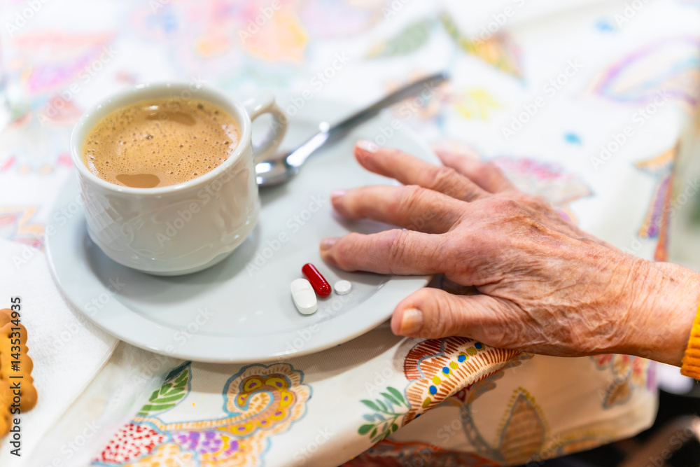 Elderly person reaching for medication with coffee and biscuits on table in nursing home