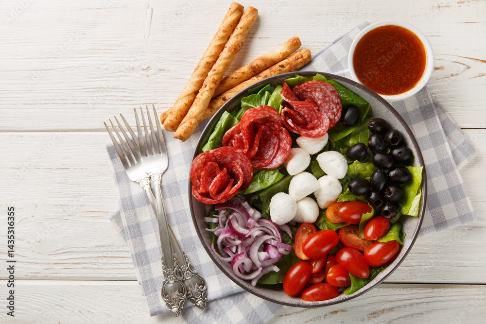 Pizza bowl salad with salami sausages, mozzarella cheese, tomatoes, olives, onions, romaine lettuce and spicy dressing served with breadsticks close-up. Horizontal top view from above