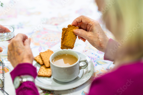 Elderly woman dunking biscuits in tea at nursing home