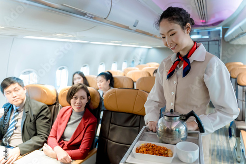 Flight attendant serving meal and beverage to passengers on airplane, providing hospitality and inflight service during commercial flight in economy class cabin photo