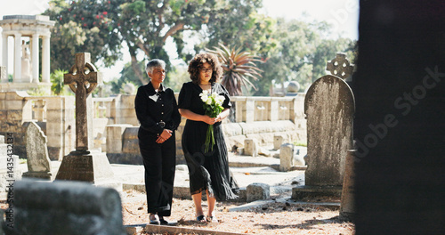 Sad, people and mourning with flowers at cemetery for death ceremony, memorial service or respect. Funeral, women or floral bouquet by tombstone for burial support, loss and grieving with remembrance