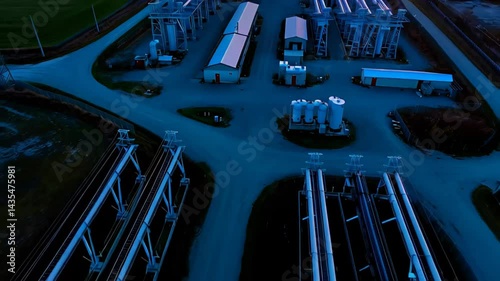 Industrial energy facility with silos, transformers and power infrastructure in rural area at sunset


