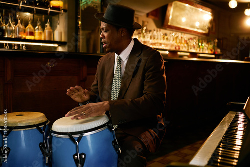 Sticker Medium shot of Black male musician in hat playing traditional conga drums, while