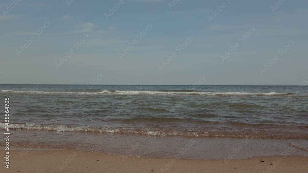 Low angle closeup shot of calm azure waves rolling on white sand of empty beach on Baltic sea coast under clear blue sky at spring day. With no people tranquil seascape natural background. Low angle closeup shot of calm azure waves rolling on white sand of empty beach on Baltic sea coast under clear blue sky at spring day. With no people tranquil seascape natural background.