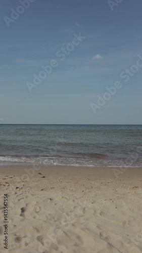 Tranquil seaside landscape of Baltic sea coast with calm azure waves rolling on empty sandy beach under clear blue sky at spring day. With no people vertical seascape natural background.