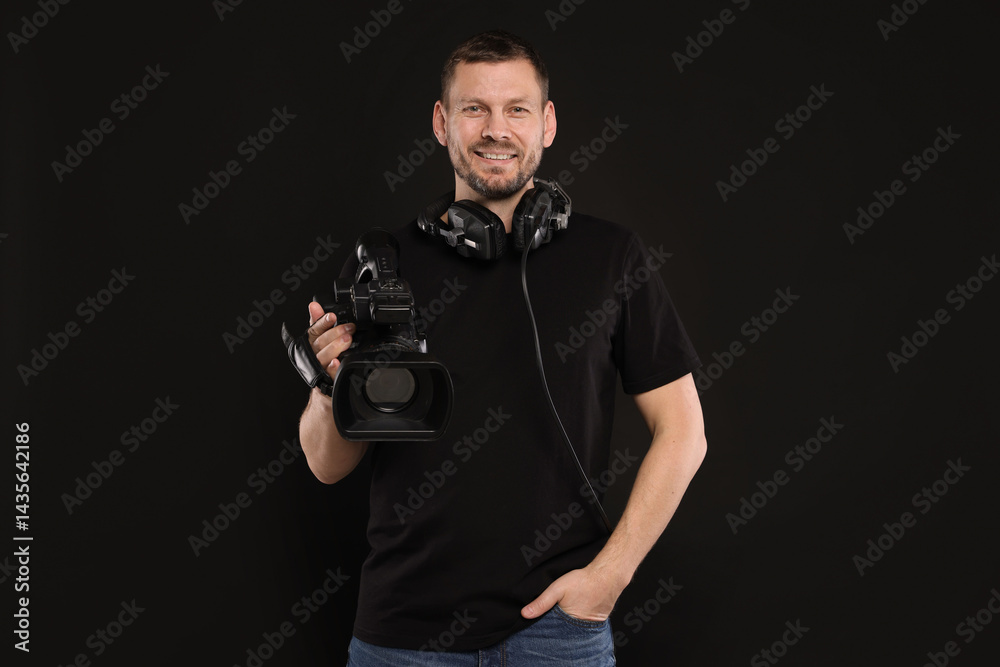 Fototapeta premium Man with professional video camera and headset on black background