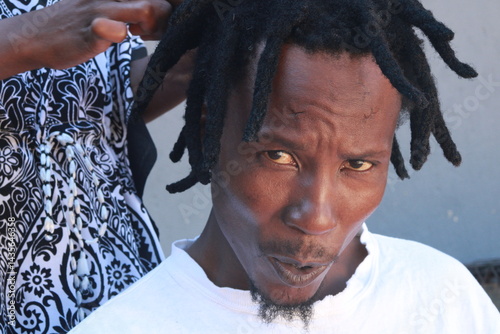 African Man with dreadlocks in a hair salon plaited by a young African lady