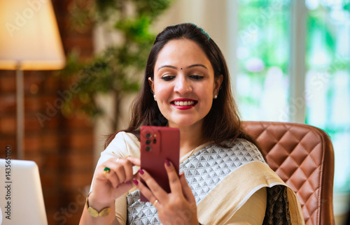 Photography Checking phone while at desk, Indian corporate lady multitasks in traditional et
