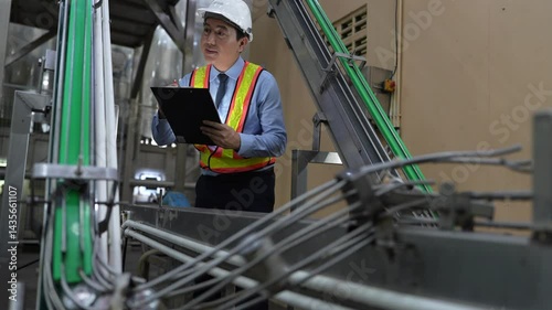 engineer in safety helmets and vests inspecting control systems inside a clean, industrial food processing plant while discussing findings on a digital tablet.