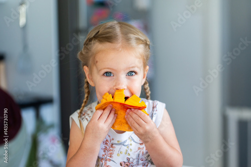 Young Australian toddler kid eating fresh mango fruit in kitchen at home during summer