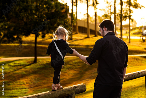 Child showing trust walking along post holding to fathers hand in golden light