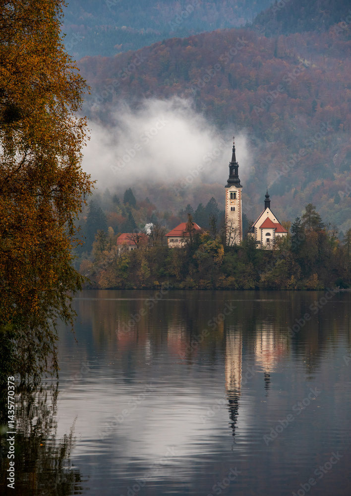 Assumption of mary pilgrimage church on lake bled, surrounded by mountains and colorful autumn foliage, in slovenia