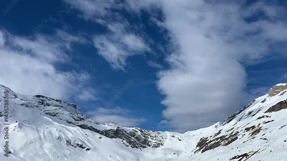 Time-lapse of snow-capped Swiss Alps and blue sky with fast-moving clouds. Natural background with mountain scenery. Winter landscape in the Engstligenalp, Adelboden region, Switzerland. Time-lapse of snow-capped Swiss Alps and blue sky with fast-moving clouds. Natural background with mountain scenery. Winter landscape in the Engstligenalp, Adelboden region, Switzerland.