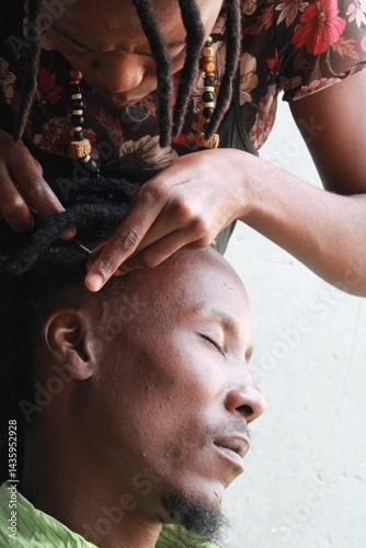 African Man with dreadlocks in a hair salon plaited by a young African lady
