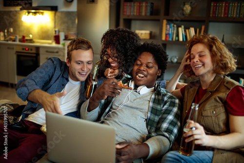 Group of friends drinking beer eating pizza and watching movie on laptop at home party