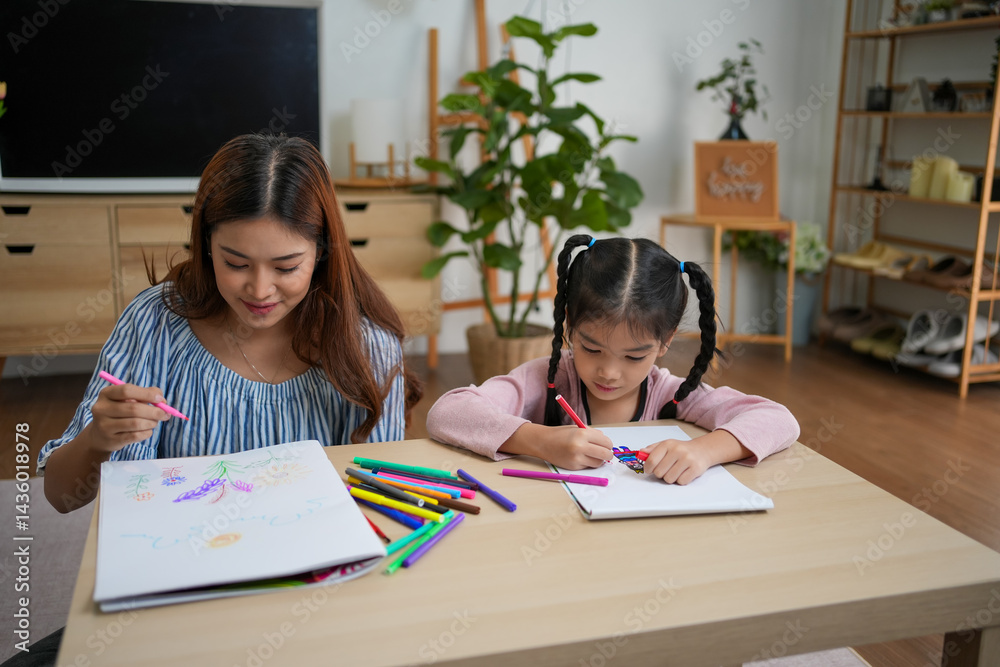 Fototapeta premium Young woman and girl happily drawing with colorful markers at wooden table in cozy living room with plants and shelves