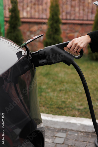Unrecognisable woman inserting EV charger plug from public or home charging station for modern electric or hybrid car at special place for e-car. Concept eco-friendly sustainability energy car