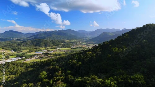 Charming countryside town nestled in lush mountains. Greenery surrounds quaint houses. Peaceful aerial view.