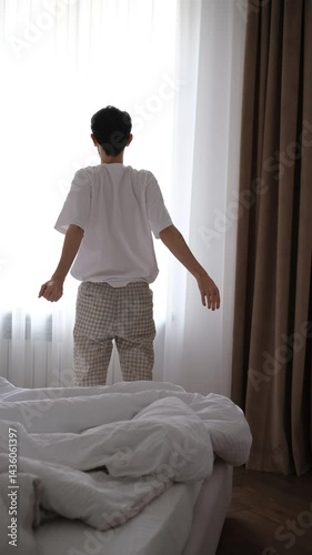 young brunette man in pajamas just woke up and stretches view from the back