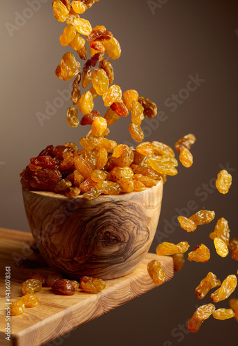 Yellow sultana raisins pour into a wooden bowl.