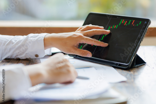 Focused on strategy, an investor holds a market analysis report, assessing stock performance with a tablet displaying real-time fluctuating graphs beside them.