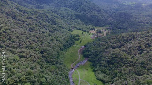 Serene river winding through green mountain valleys. Lush vegetation blankets the landscape. Peaceful flight over nature's beauty