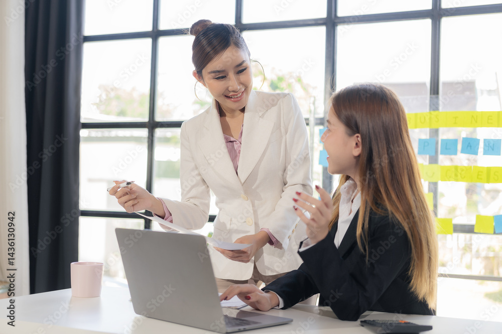 Obraz premium Two Asian businesswomen are discussing their business. While pointing at the graphs and charts on the table, enjoy the success and teamwork in business analysis.