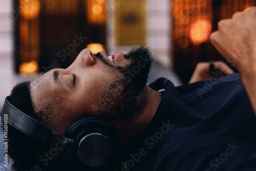 Photos Bearded man lies calmly with headphones, listening to music with closed eyes, so