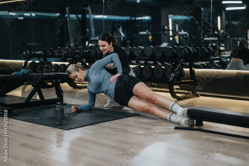 Obraz na płótnie A coach provides guidance to a woman performing a side plank on a mat, focusing on proper form and fitness in a contemporary gym environment. w salonie