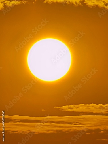 A golden sun shining brightly in a clear winter sky, with icicles in the foreground., Full sun is setting in the sky