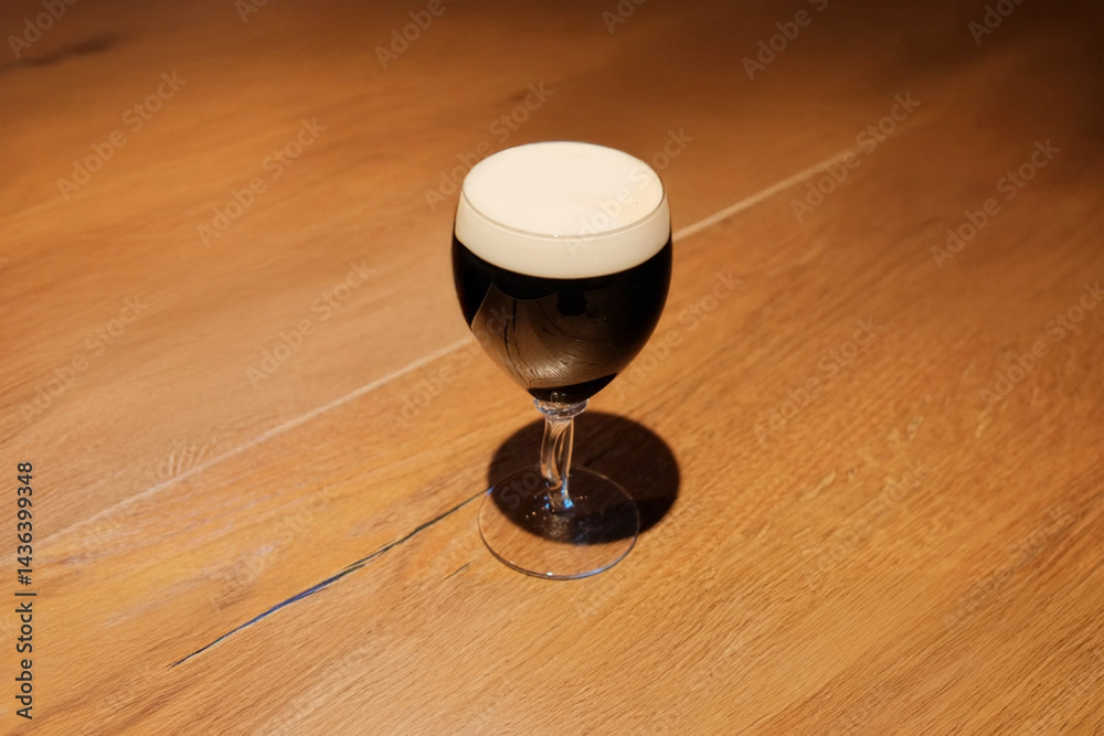 Glass of dark stout beer with a creamy foam head on a wooden table under warm lighting Glass of dark stout beer with a creamy foam head on a wooden table under warm lighting