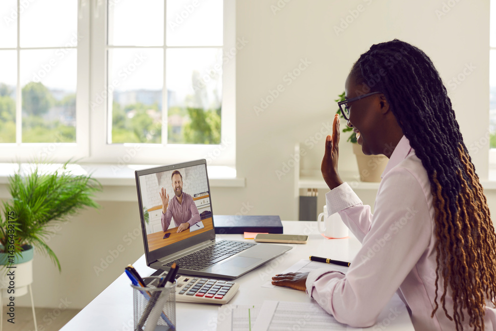 Diverse business woman and man having online work meeting via video call. Happy African American woman financial accountant sitting at her office desk, smiling and waving hello at laptop computer