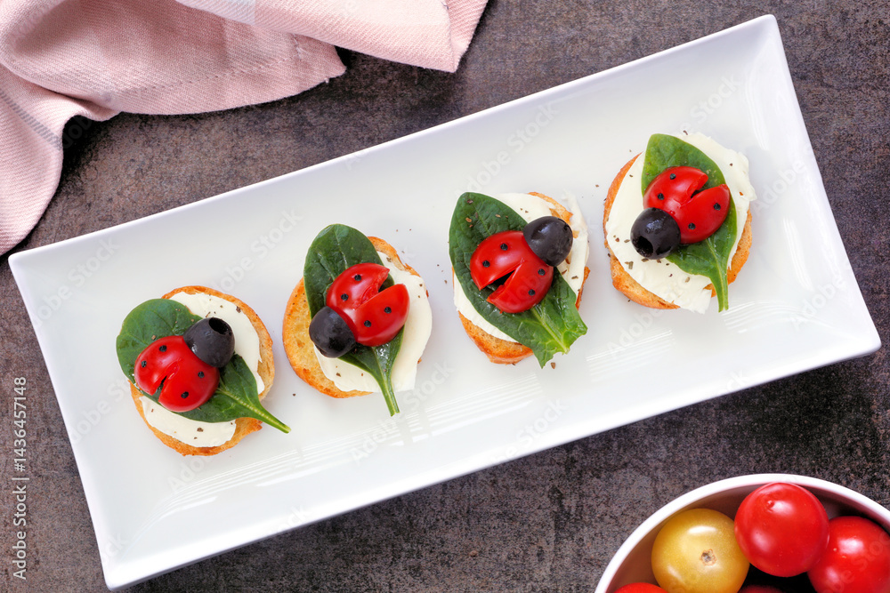 Fun summer theme ladybug crostini appetizers. Top view table scene against a white wood background. Top view.