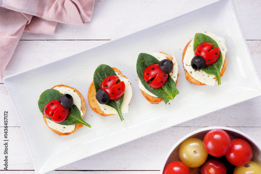 Fun summer theme ladybug crostini appetizers. Top view table scene against a dark background. Above view.