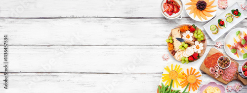 Summer garden party food side border. Variety of fun flower theme charcuterie items, cheese, fruit, vegetables and finger snacks. Top view on a white wood banner background.