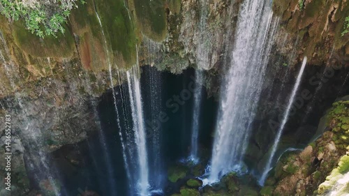 Cascading waterfall tumbling through lush moss-draped canyon, turquoise waters flowing between weathered rocky cliffs in untouched wilderness setting