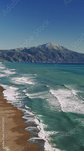 Aerial view capturing rolling waves washing over sandy shoreline, mountain silhouettes creating serene coastal scenery with pristine natural beauty