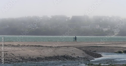 Distant figures on isolated beach misty sea spray in air