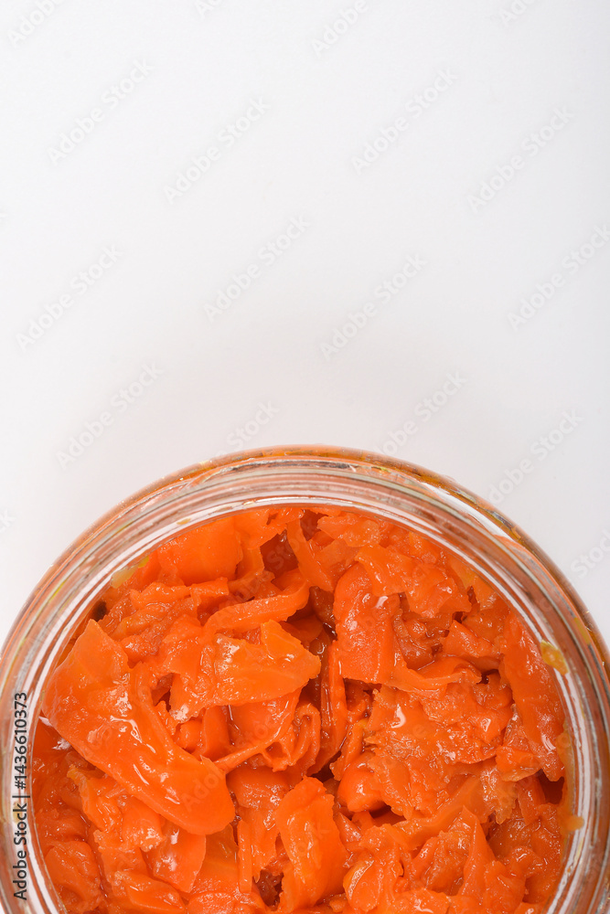 An overhead close-up shows a clear glass jar filled with vibrant orange, thinly sliced carrots prepared as vegan salmon against a plain white background