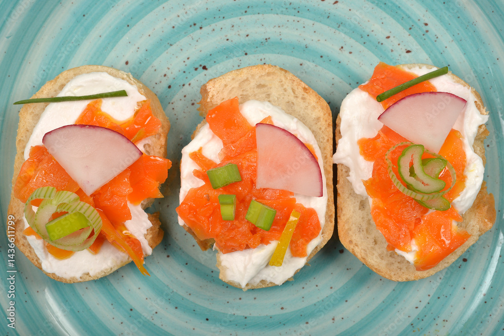 An overhead view shows three elegant canapes with a creamy spread, vibrant orange carrot prepared as vegan salmon, radish slices, and green chives on a light blue swirled plate