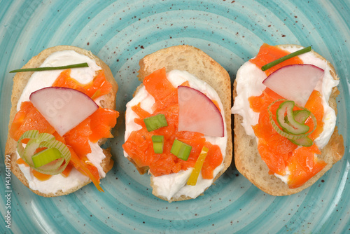 Obraz na płótnie An overhead view shows three elegant canapes with a creamy spread, vibrant orange carrot prepared as vegan salmon, radish slices, and green chives on a light blue swirled plate w salonie
