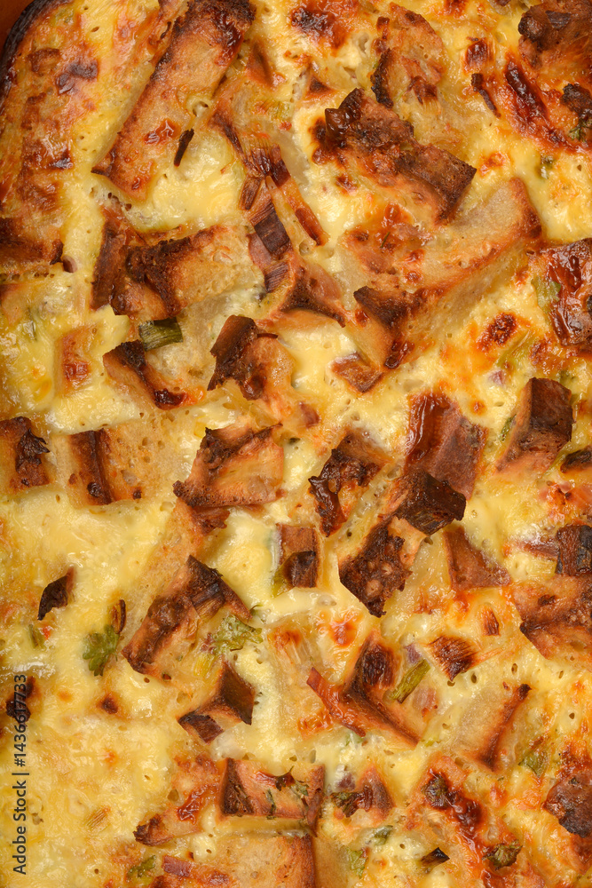 A close-up shot reveals the golden-brown, bubbly surface of a freshly baked strata (layered casserole dish made from a mixture which mainly consists of bread, eggs and cheese)