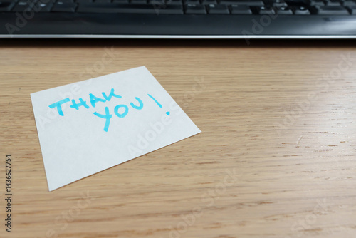 Handwritten thank you card placed near laptop keyboard, signaling appreciation in professional workspace. Sticky notes