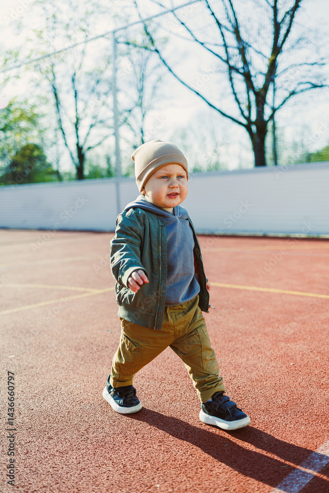 Toddler boy running outside with soap bubbles. Child on a warm spring day for a walk in a jacket and hat.